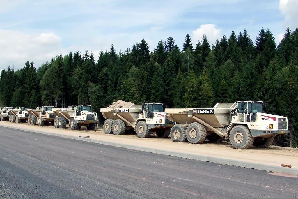 Row of articulated dump trucks parked along a newly paved road at a construction site