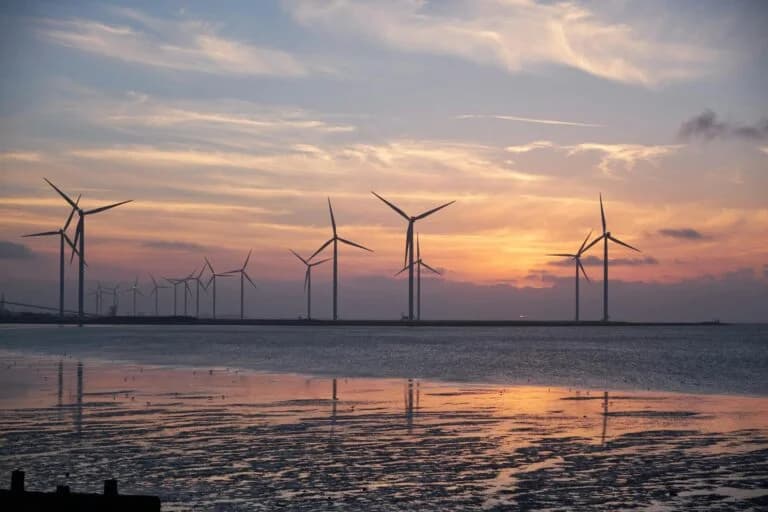 Row of wind turbines along the coast at sunset, reflected in the wet sand