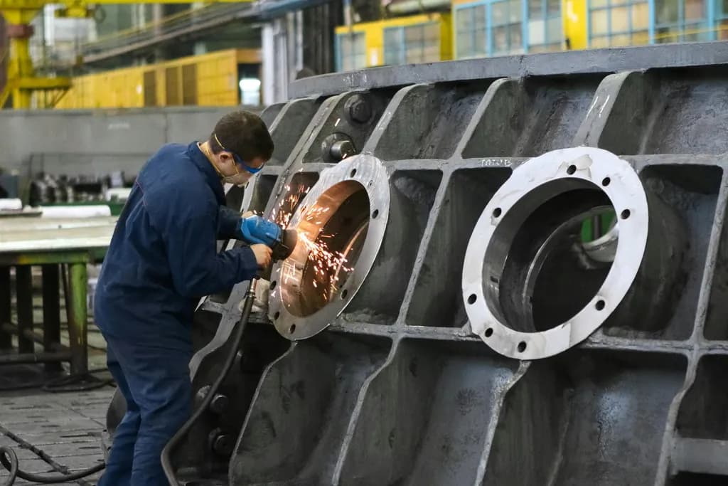 Factory worker in safety glasses grinding a large metal casting as sparks fly on the plant floor