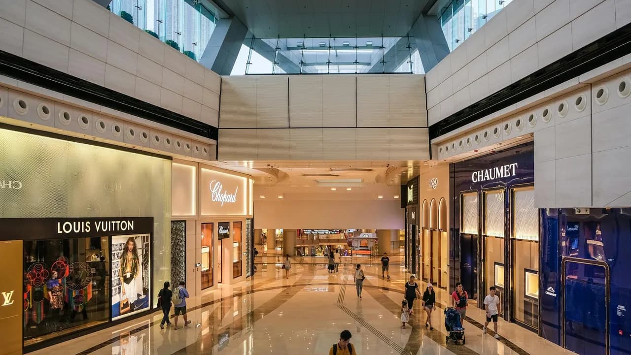 Bright indoor shopping mall walkway lined with storefronts and shoppers