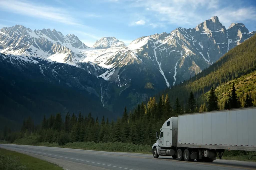 Semi truck driving along a highway through a forested mountain valley